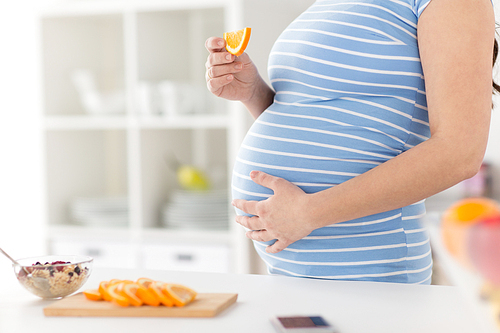 pregnancy, healthy food and people concept - close up of pregnant woman eating orange breakfast at home kitchen