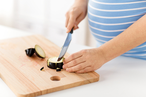 pregnancy, cooking food and healthy eating concept - close up of pregnant woman with kitchen knife chopping eggplant at home