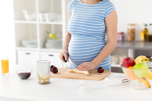 cooking, pregnancy and healthy eating concept - pregnant woman with kitchen knife chopping fruits on wooden cutting board at home