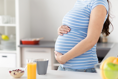 pregnancy, healthy eating and maternity concept - close up of pregnant woman touching her belly with breakfast on kitchen table at home