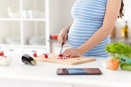 pregnancy, cooking food and healthy eating concept - close up of pregnant woman with kitchen knife chopping radish on wooden cutting board at home