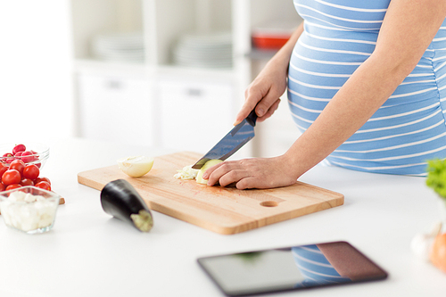 pregnancy, cooking food and healthy eating concept - close up of pregnant woman with kitchen knife chopping onion at home