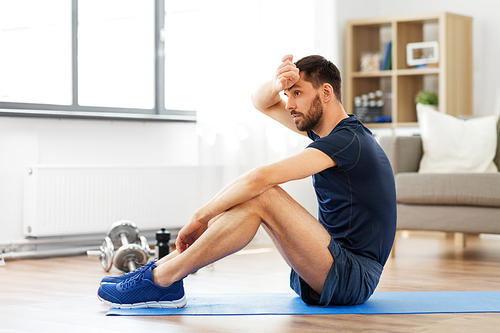 sport, fitness and healthy lifestyle concept - tired man sitting on exercise mat at home