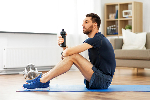 sport, fitness and healthy lifestyle concept - man drinking water from bottle during training at home