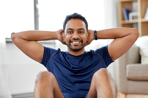 sport, fitness and healthy lifestyle concept - smiling indian man making abdominal exercises at home