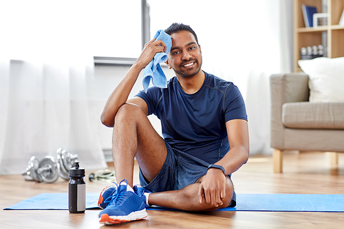 fitness, sport and healthy lifestyle concept - smiling but tired indian man wiping face with towel after training at home