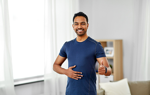 sport and healthy lifestyle concept - smiling indian man with fitness tracker showing thumbs up at home
