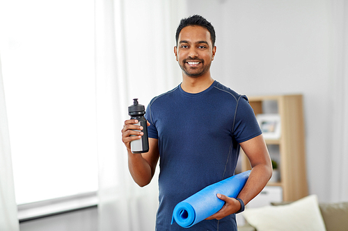 fitness, sport and healthy lifestyle concept - smiling indian man with exercise mat and bottle of water or energy drink at home