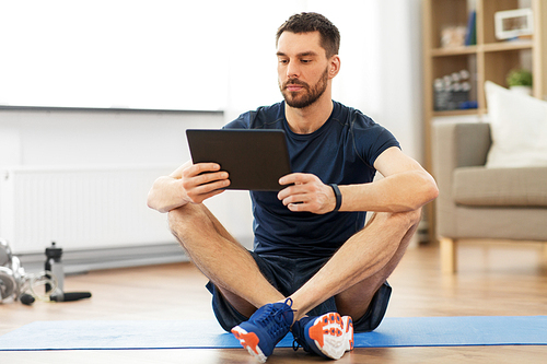 sport, fitness and healthy lifestyle concept - man with tablet computer sitting on exercise mat at home