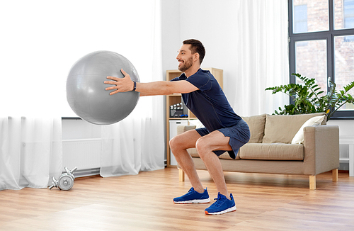 fitness, sport and healthy lifestyle concept - smiling man exercising and doing squats with ball at home