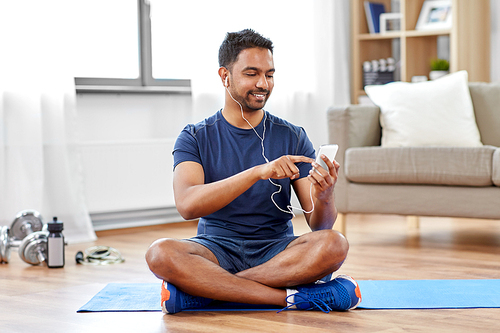 sport, technology and healthy lifestyle concept - smiling indian man in earphones listening to music on smartphone at home