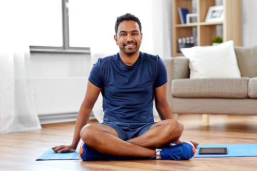 sport and healthy lifestyle concept - smiling indian man sitting on exercise mat at home