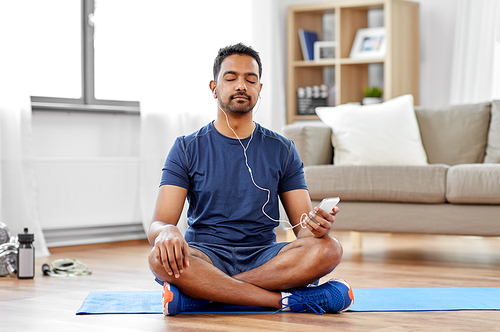 sport, technology and healthy lifestyle concept - indian man in earphones listening to music on smartphone at home