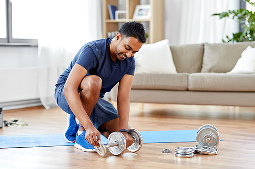 fitness, sport, weightlifting and bodybuilding concept - smilingindian man assembling dumbbells at home