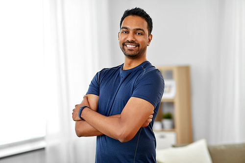 sport and healthy lifestyle concept - smiling indian man with fitness tracker and crossed arms at home