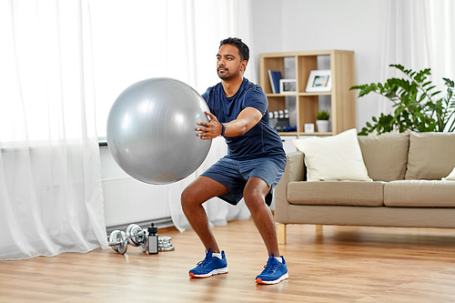 fitness, sport and healthy lifestyle concept - indian man exercising and doing squats with ball at home