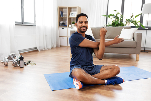 sport, fitness and healthy lifestyle concept - indian man training and stretching arm at home