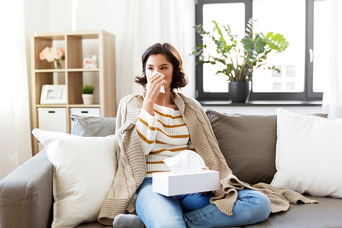 healthcare, cold, hygiene and people concept - sick woman blowing her runny nose in paper tissue at home