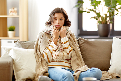 people, health and cold concept - sad sick woman in blanket and scarf at home