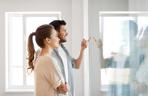 mortgage, people and real estate concept - happy couple looking through window at new home