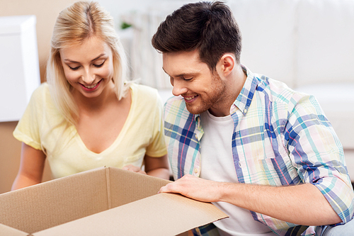 mortgage, moving and real estate concept - happy couple looking inside box or parcel at home