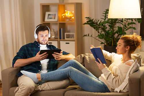 leisure and people concept - couple with tablet computer, headphones and book at home in evening