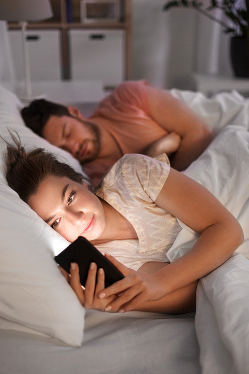 technology, internet addiction and cheat concept - woman using smartphone at night while her boyfriend is sleeping