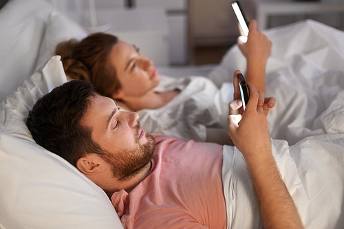 technology, internet and communication concept - couple using smartphones in bed at night