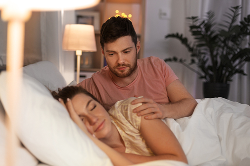 people, rest and relationships concept - man waking his sleeping wife up in bed at home