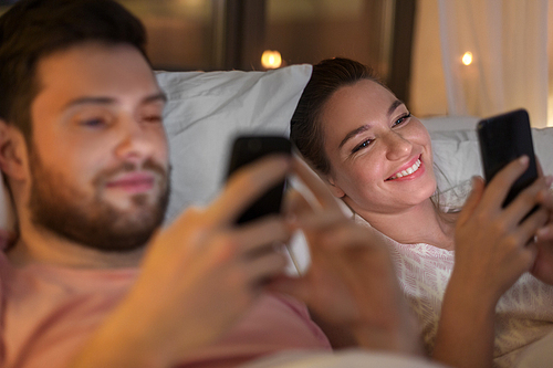 technology, internet and communication concept - couple using smartphones in bed at night