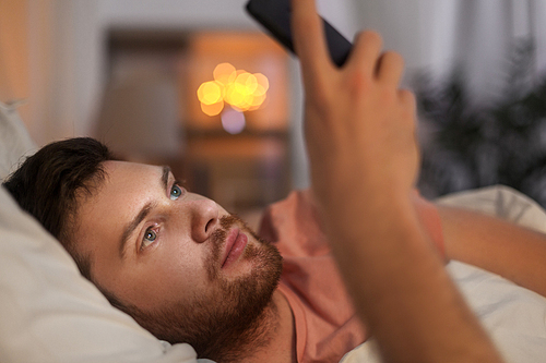 technology, internet addiction and people concept - young man using smartphone in bed at home at night