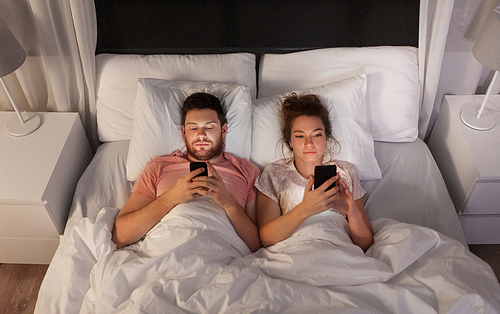 technology, internet and communication concept - couple using smartphones in bed at night