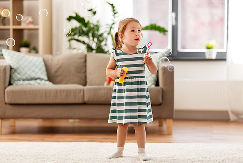 childhood and family concept - little girl blowing soap bubbles at home