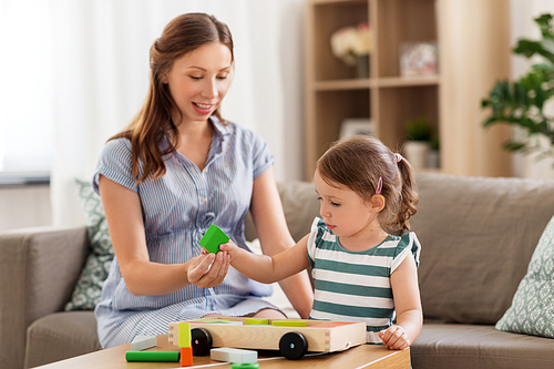 childhood and people concept - happy pregnant mother and little daughter playing with toy blocks at home