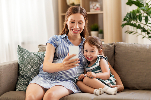 pregnancy, people and family concept - happy pregnant mother and little daughter with smartphone at home