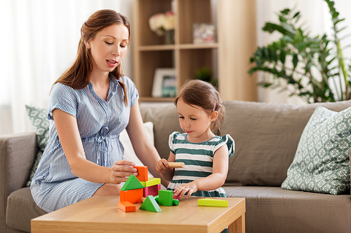 childhood and people concept - happy pregnant mother and little daughter playing with toy blocks at home