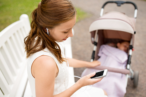 motherhood, technology and people concept - close up of happy mother with smartphone, earphones and baby in stroller listening to music at summer park