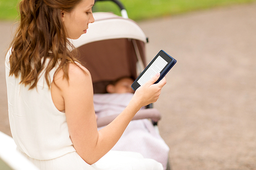 motherhood, leisure and technology concept - close up of mother with child in stroller reading internet book at summer park