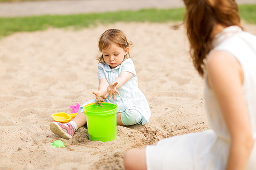 childhood, leisure and people concept - little baby girl plays with toys in sandbox