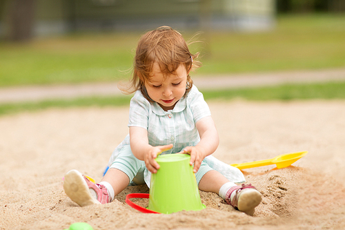 childhood, leisure and people concept - little baby girl plays with toys in sandbox