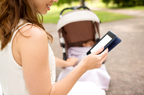 motherhood, leisure and technology concept - close up of happy mother with child in stroller reading internet book at summer park