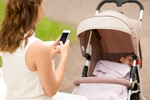 motherhood, technology and people concept - close up of mother with smartphone and baby girl in stroller at summer park