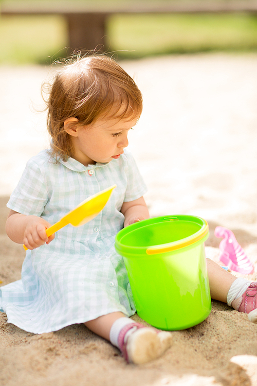 childhood, leisure and people concept - little baby girl plays with toys in sandbox