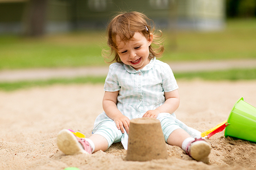 childhood, leisure and people concept - little baby girl plays with toys in sandbox