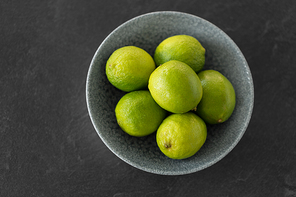 food, healthy eating and vegetarian concept - close up of whole limes in bowl on slate table top