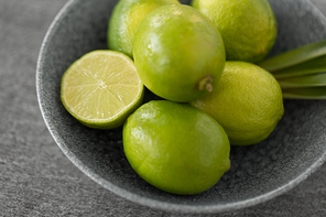 food, healthy eating and vegetarian concept - close up of limes in bowl on slate table top