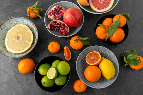 food, healthy eating and vegetarian concept - close up of citrus fruits in bowls on stone table