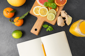 food, healthy eating and vegetarian concept - close up of citrus fruits, wooden cutting board and notebook on slate table top