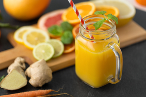 food , healthy eating and vegetarian concept - mason jar glass of orange juice with straw and citrus fruits on slate table top