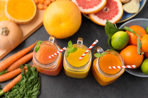 food , healthy eating and vegetarian concept - mason jar glasses of orange and carrot juices with paper straws, fruits and vegetables on slate table